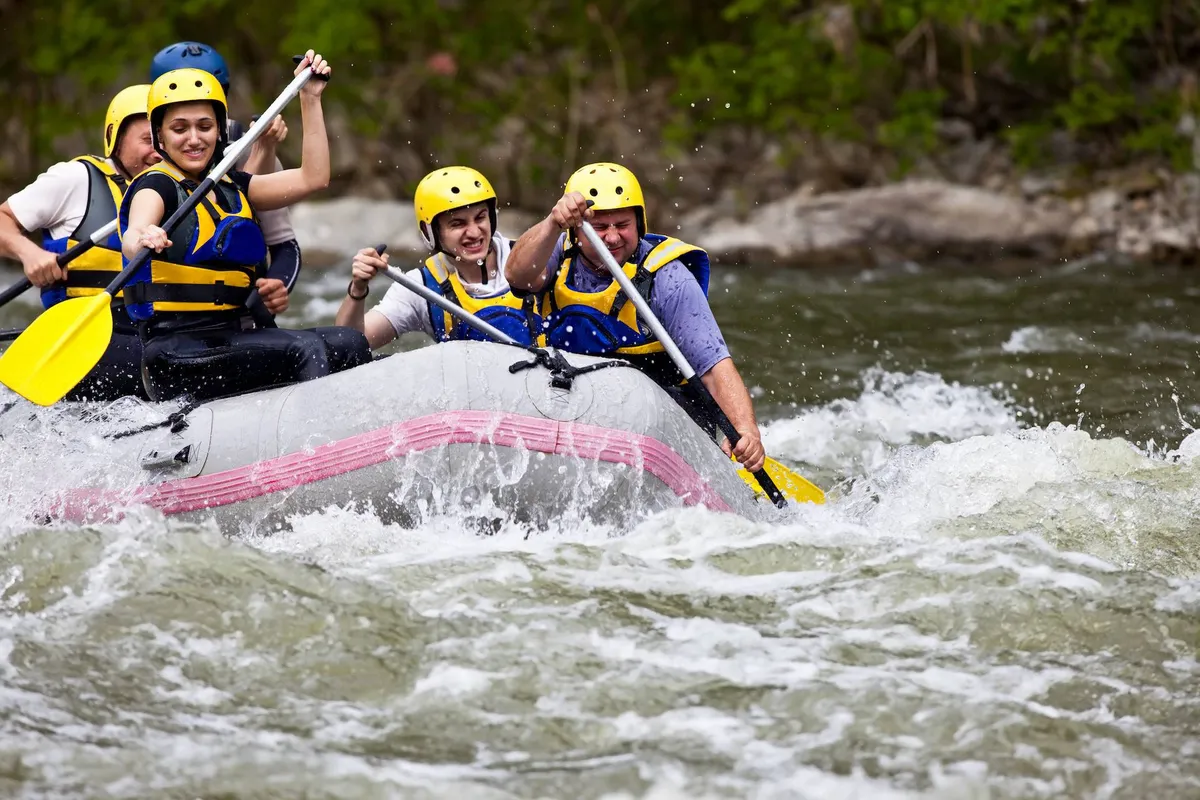 An exciting scene of a group of people whitewater rafting on a lively river, paddles in hand, working together as they navigate the rapids. The image is full of motion and camaraderie, with water splashing under bright daylight.