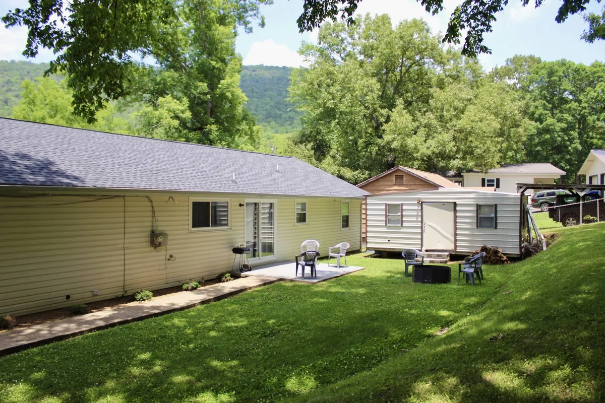 A welcoming view of the house exterior featuring a spacious patio area, ample greenery, and scenic mountain vistas in the background. The patio includes comfortable seating, perfect for relaxing after outdoor adventures, and the surrounding nature creates a tranquil setting for both guests and their pets.