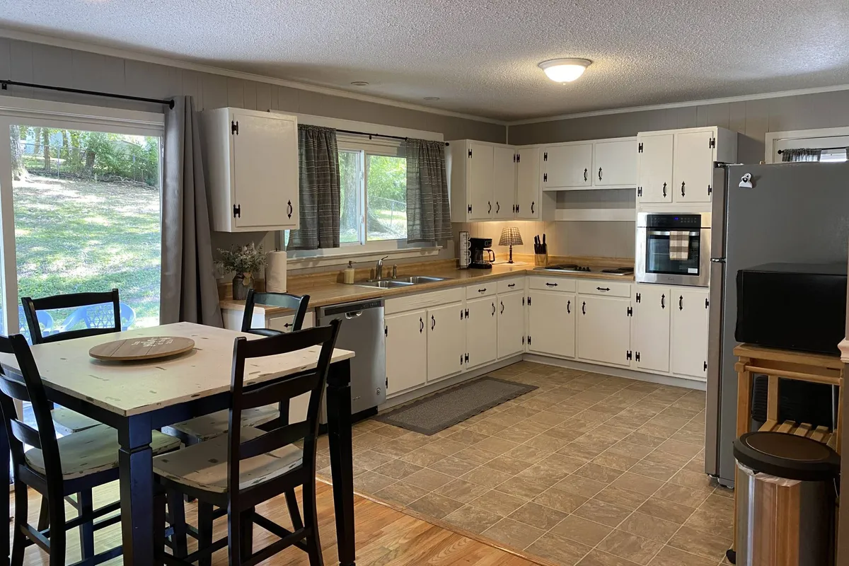 This image showcases a modern kitchen area with a central island, large windows that let in ample natural light, and sleek cabinetry. The scene evokes warmth and togetherness, suggesting a space ready for cooking and gathering. Stainless steel appliances are visible, contributing to the kitchen's contemporary feel.
