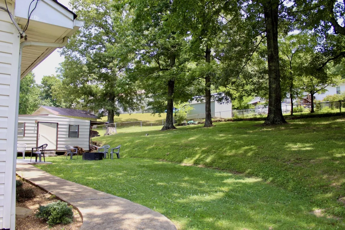 A lush green lawn shaded by mature trees, with an inviting outdoor seating area and a gentle pathway. The scene exudes tranquility and the promise of relaxation in a private, serene setting.