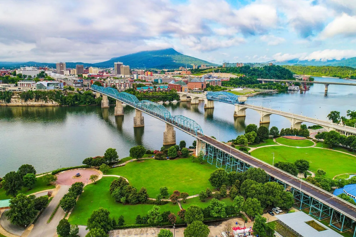A sweeping view of Chattanooga’s iconic blue bridge spanning the river, with the city skyline and surrounding mountains in the background. The scene captures the energy and vibrancy of the city, inviting outdoor exploration and sightseeing.