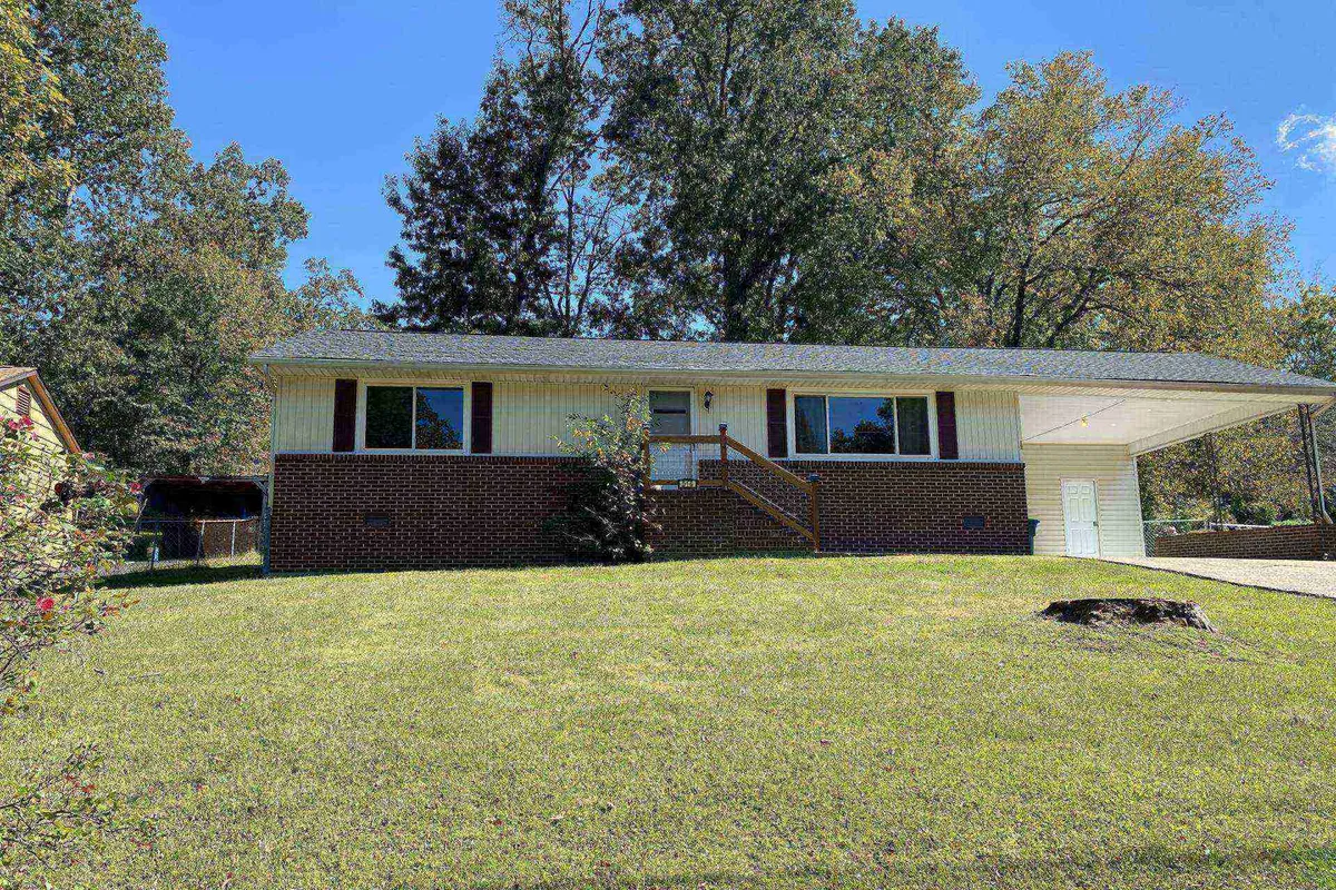 A welcoming exterior view of the home, highlighting the spacious front porch, large windows, green lawn, and mature surrounding trees. The setting feels open and inviting, perfect for gatherings or relaxing before and after a day of adventure.