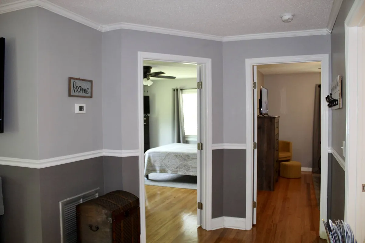 A welcoming entryway and connected living space featuring wooden floors, doorways, and a decorative sign, creating an inviting transition point between the home and the outdoors. The area is designed for gathering and welcoming guests after a day of exploration.